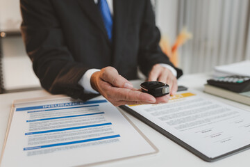 A businessman in a formal suit explains car insurance details, holding a small red car model and pointing at contract documents, symbolizing agreement, protection, and financial planning.