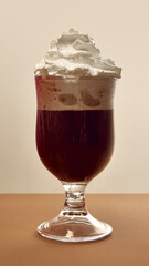 Coffee with whipped cream foam in glass on neutral beige background under warm light. Concept of cafe branding, culinary indulgence, beverage advertising, and elegant lifestyle design.