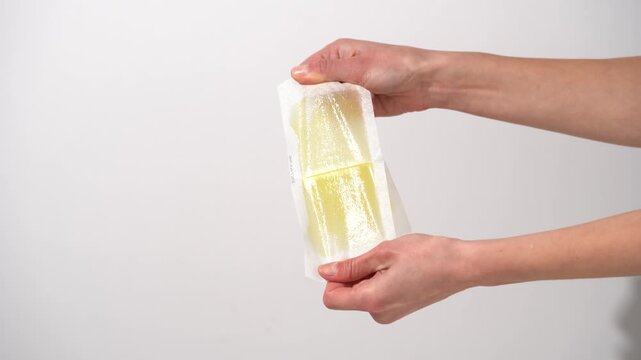 Young woman's hands uncover two sticky yellow hair removal tapes on a white isolated background. Concept of waxing strips is based on the adhesion of wax to hair and its removal from the root.