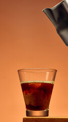Coffee in glass with rich swirl texture and metal pitcher above against warm background. Concept of barista craft, beverage creation, cafe design, and culinary branding.