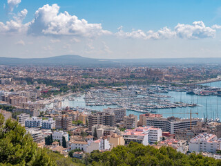 A panoramic view of Palma de Mallorca city with a harbor filled with boats, set against a backdrop of rolling hills and a clear blue sky, Majorca