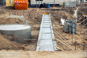 Concrete foundation poured into metal formwork at construction site. Steel rods, braces and rebar elements create strong structure supported by soil and wooden beams