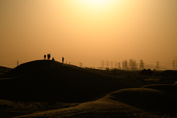 Silhouette of five people standing on a stand dune with electricity power lines in the distance at sunset, Dubai, UAE