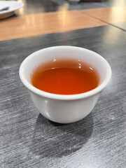 A close-up of a cup of hot tea served in a white ceramic cup on a wooden table