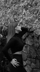 A woman in a black crop top and wide-leg pants stands by a stone wall on the steps in a park. She has her head thrown back and is relaxedly breathing in the fresh air, enjoying a moment of peace.