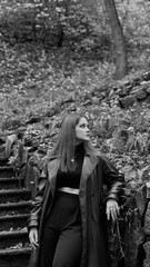 A woman in a black crop top and wide-leg pants stands by a stone wall on the steps in a park. She has her head thrown back and is relaxedly breathing in the fresh air, enjoying a moment of peace.