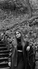 A woman in a black crop top and wide-leg pants stands by a stone wall on the steps in a park. She has her head thrown back and is relaxedly breathing in the fresh air, enjoying a moment of peace.