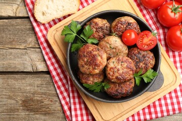 Delicious patties with parsley, tomatoes and bread on wooden table, top view