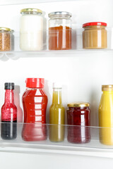 Bottles with different tasty sauces in fridge, closeup