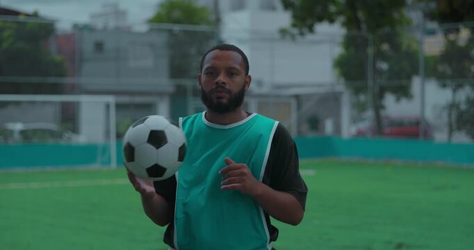 Hispanic man of African descent holding soccer ball and looking directly at camera on turf field, calm portrait showing focus, confidence and determination during outdoor training