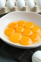 Raw eggs and yolks in bowl on table, closeup