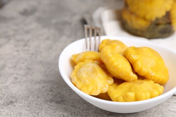 Pickled pattypan squashes in bowl and fork on grey textured table, closeup. Space for text