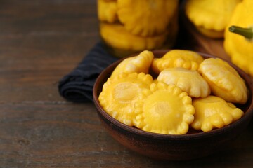 Pickled pattypan squashes in bowl on wooden table, closeup. Space for text