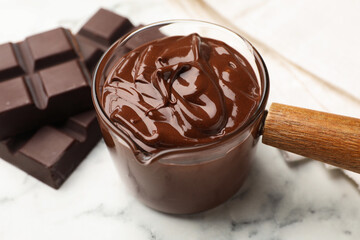 Melted chocolate and pieces on white marble table, closeup
