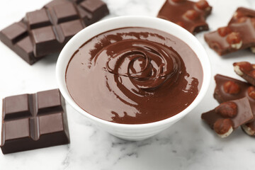 Bowl with melted chocolate and pieces on white marble table, closeup