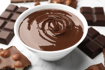 Bowl with melted chocolate and pieces on white marble table, closeup