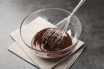 Fototapeta premium Bowl with melted chocolate and whisk on grey table, closeup