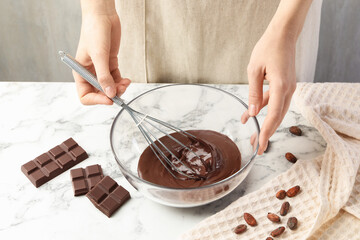 Woman mixing melted chocolate in bowl at white table, closeup
