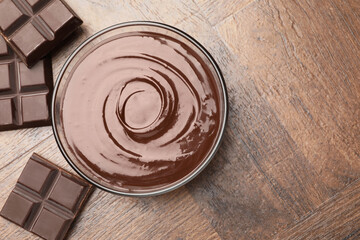 Bowl with melted chocolate and pieces on wooden table, flat lay. Space for text