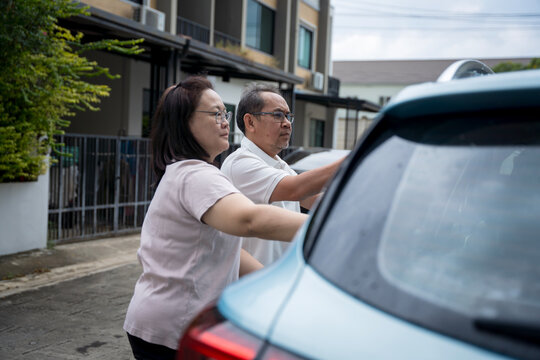 Middle aged Asian couple enjoys quality time together washing their blue car on a sunny day