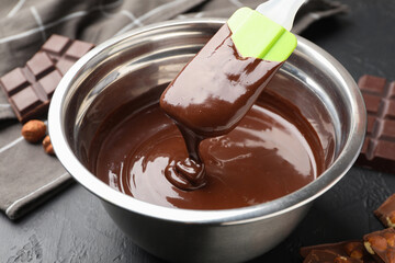 Melted chocolate and pieces with hazelnuts on black table, closeup