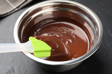 Melted chocolate and spatula in bowl on black table, closeup