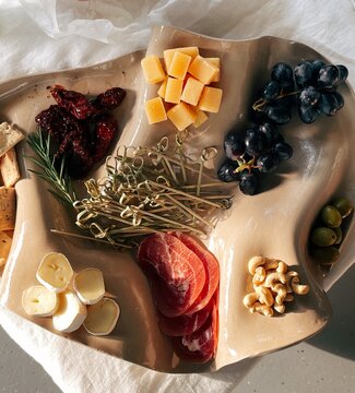 Overhead view of a cheese and charcuterie board with grapes, olives, cashew nuts, bread and sun dried tomatoes on a table