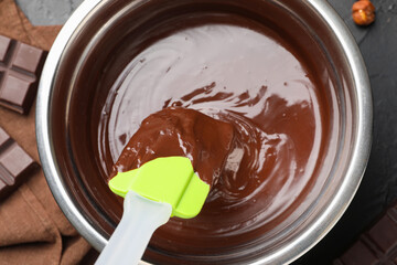 Melted chocolate and spatula in bowl on black table, top view