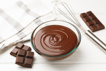 Melted chocolate, whisk and pieces white on wooden table, closeup