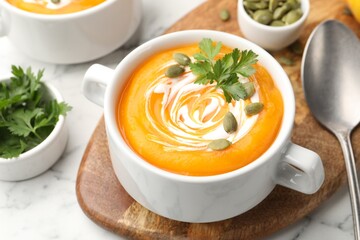 Tasty pumpkin cream soup with parsley and seeds served on light marble table, closeup