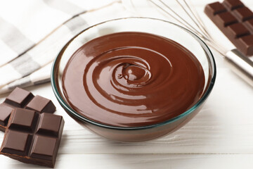 Melted chocolate, whisk and pieces white on wooden table, closeup