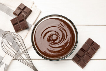 Melted chocolate, whisk and pieces white on wooden table, flat lay