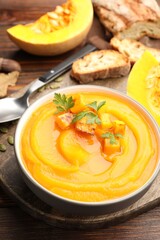 Delicious pumpkin cream soup with parsley served on wooden table, closeup