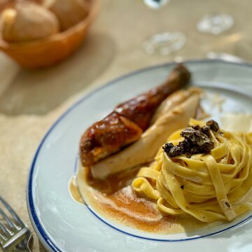 Close-up of roast chicken and tagliatelle pasta with fresh morel mushrooms on a table with a basket of bread rolls