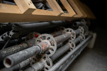Stack of metal scaffolding parts stored with wooden planks above creates industrial composition. Scratched steel surfaces show signs of use and construction work preparation