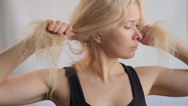 Beautiful woman with messed up hair. Unhappy grimacing face. Blond bleaching hairstyle with problem brittle hair. Split ends of bleached hair. Hairstyle, daily beauty routine. Cosmetic and trichology