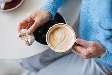 Overhead view of a woman sitting at a table eating a vanilla and coconut macaron and drinking a cappuccino