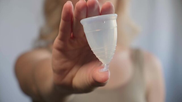 Close-up woman shows menstrual cup in hand. Feminine hygiene products, environmental responsibility and self-awareness. Daily care and the female cycle. Eco in women health, menstruation or period