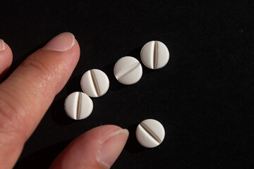 White pills on black background with fingers close-up