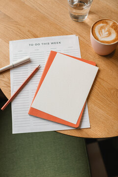 Close-up of a to do list on a table with a notebook, pen, pencil, cappuccino and glass of water