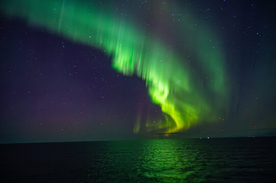A mesmerizing display of the Northern Lights illuminates the night sky over the ocean, creating a vibrant, glowing arc against the dark backdrop