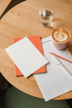 Close-up of a to do list on a table with a notebook, pen, pencil, cappuccino and glass of water