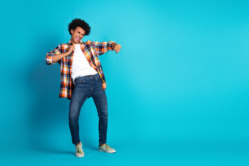 Young man dancing in a colorful plaid shirt on a blue studio background joyful and stylish