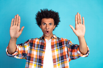 Young man with colorful plaid shirt raises hands in surprise against bright blue background stock photo