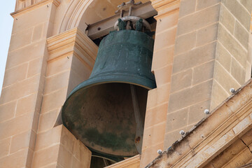 Obraz premium A large, ancient-looking bell with green patina hangs within a stone bell tower, featuring intricate carvings on its upper rim.