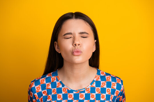 Young woman with kissy face in vibrant checkered shirt against bright yellow background for fashion lifestyle stock photo