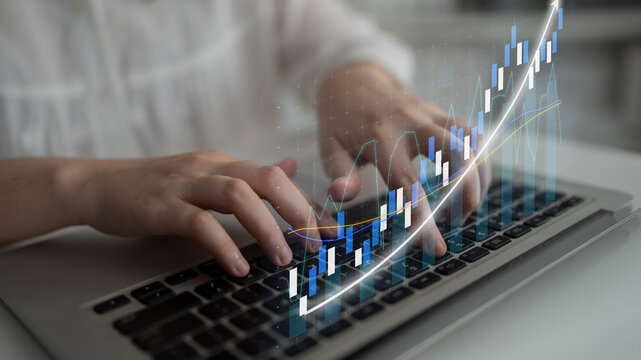 Hands actively typing on a laptop show a digital financial chart overlay, representing growth and investment strategies in a modern business environment. Impute