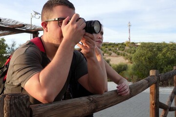 Man and woman using a camera on a wooden fence to photograph the natural landscape at sunset. Concept of photography, creativity, and teamwork.
