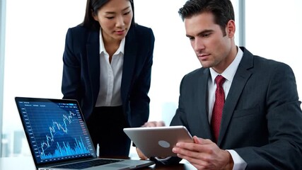 Business colleagues in suits review market data on a laptop and tablet, strategizing - Powered by Adobe