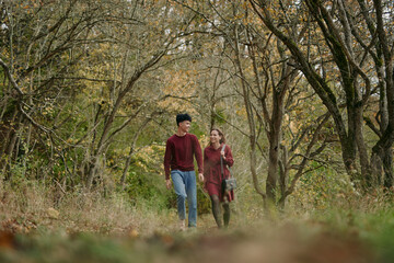 Candid couple walking along an autumn forest path, sharing an authentic, trustworthy connection and natural smiles; relaxed poses and genuine interaction capture a realistic outdoor lifestyle scene.